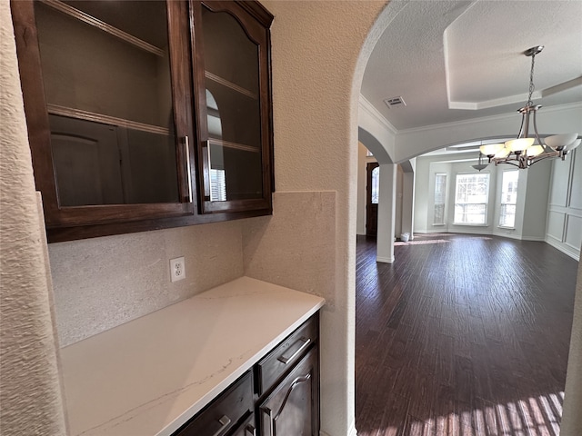 kitchen with dark brown cabinets, a textured ceiling, ornamental molding, dark hardwood / wood-style flooring, and a raised ceiling