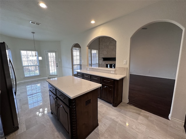 kitchen with black refrigerator, decorative light fixtures, a center island, and dark brown cabinets