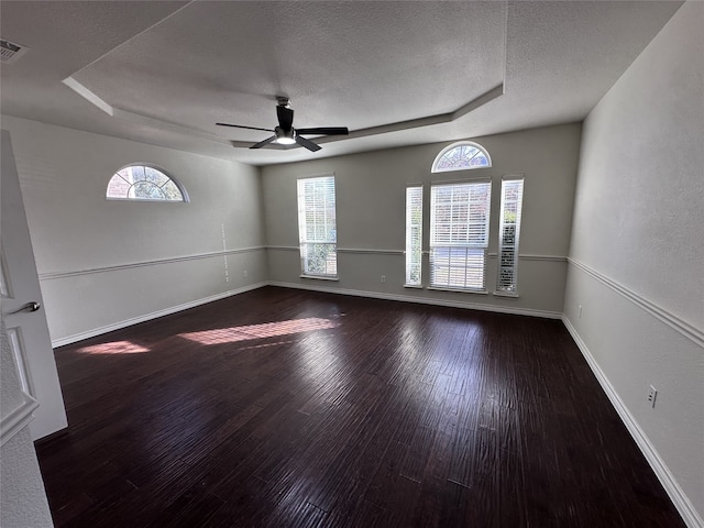 unfurnished room with ceiling fan, a tray ceiling, dark hardwood / wood-style flooring, and a textured ceiling