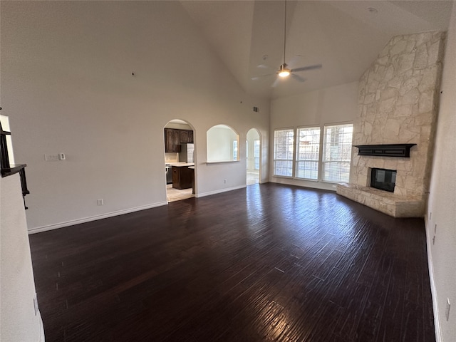 unfurnished living room featuring a stone fireplace, high vaulted ceiling, dark hardwood / wood-style floors, and ceiling fan