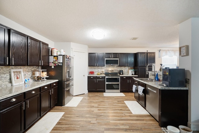 kitchen with sink, dark brown cabinets, light hardwood / wood-style flooring, appliances with stainless steel finishes, and backsplash