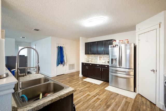 kitchen featuring tasteful backsplash, sink, light wood-type flooring, stainless steel fridge, and a textured ceiling