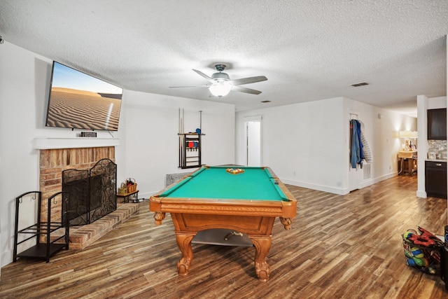 rec room with hardwood / wood-style flooring, billiards, ceiling fan, a textured ceiling, and a brick fireplace