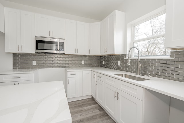 kitchen with white cabinetry, sink, backsplash, light stone counters, and light hardwood / wood-style floors