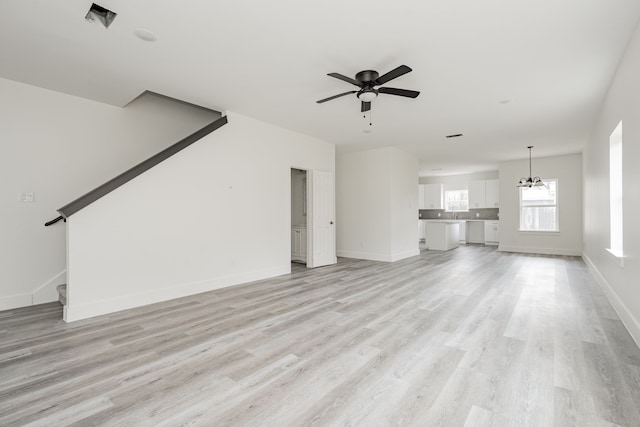 unfurnished living room with ceiling fan with notable chandelier and light hardwood / wood-style floors