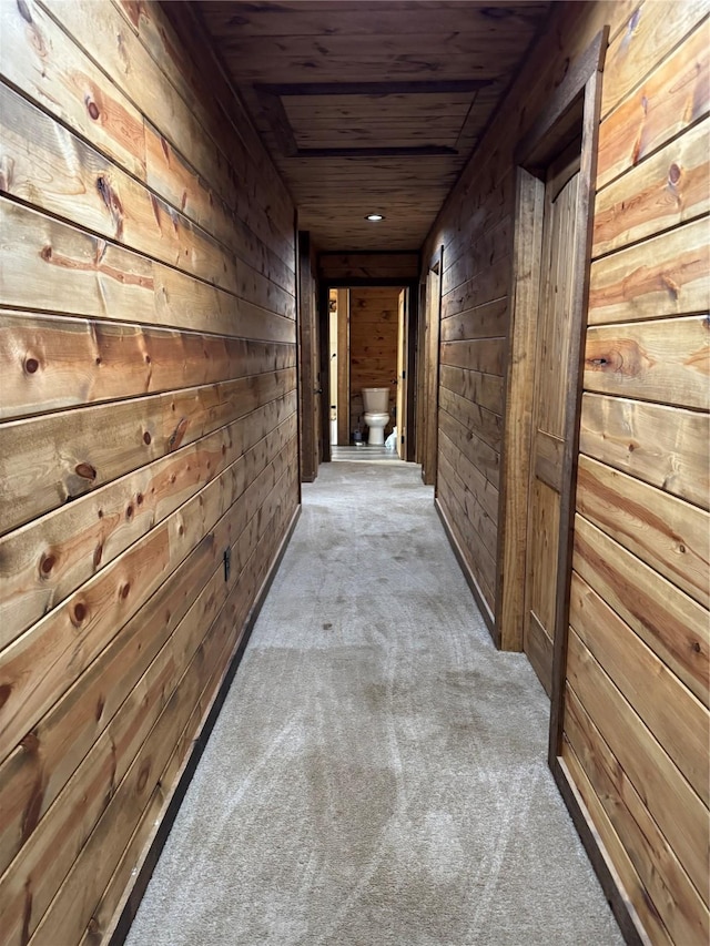 corridor featuring light carpet, wooden ceiling, and wood walls