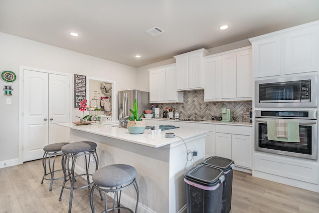 kitchen featuring a kitchen island with sink, stainless steel appliances, light hardwood / wood-style floors, and white cabinets