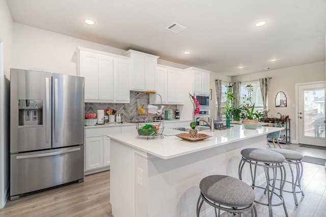 kitchen featuring built in microwave, an island with sink, white cabinetry, stainless steel refrigerator with ice dispenser, and light wood-type flooring