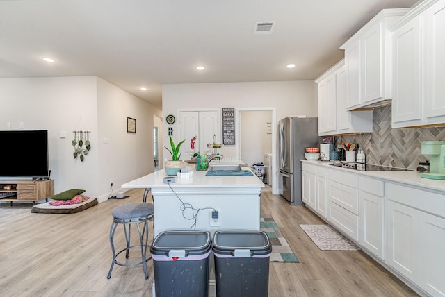 kitchen featuring stainless steel refrigerator, black electric stovetop, a center island with sink, and white cabinets