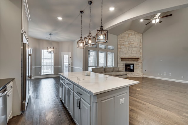 kitchen with a stone fireplace, wood-type flooring, a center island, hanging light fixtures, and light stone countertops