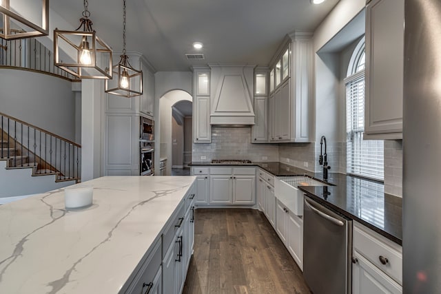 kitchen featuring premium range hood, appliances with stainless steel finishes, decorative light fixtures, white cabinetry, and dark stone counters