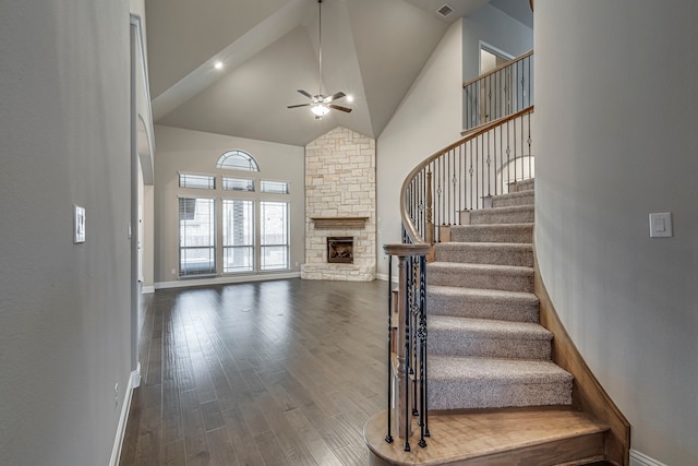 staircase featuring hardwood / wood-style floors, a fireplace, high vaulted ceiling, and ceiling fan