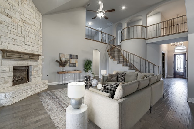 living room featuring lofted ceiling, a stone fireplace, dark wood-type flooring, and ceiling fan with notable chandelier