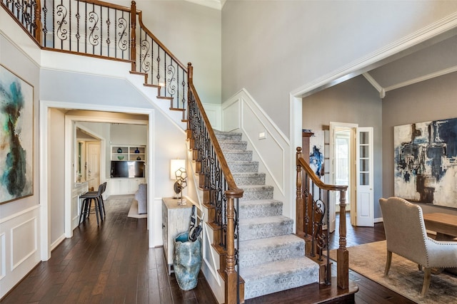 staircase featuring a high ceiling, wood-type flooring, ornamental molding, and built in features