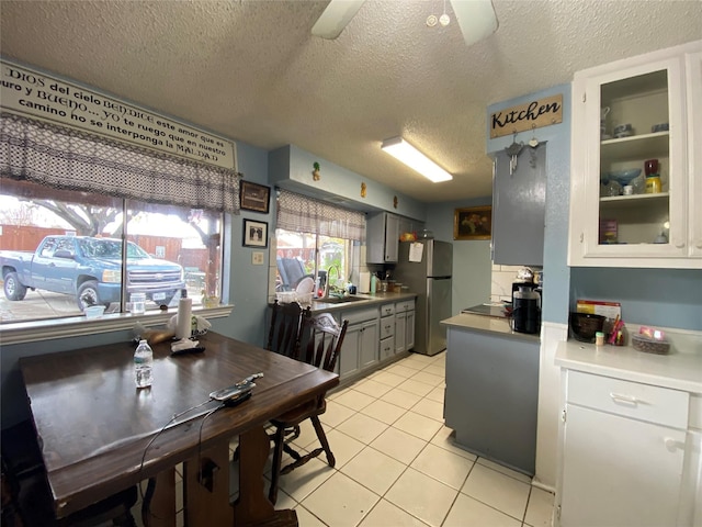 kitchen with sink, light tile patterned floors, gray cabinets, stainless steel refrigerator, and a textured ceiling