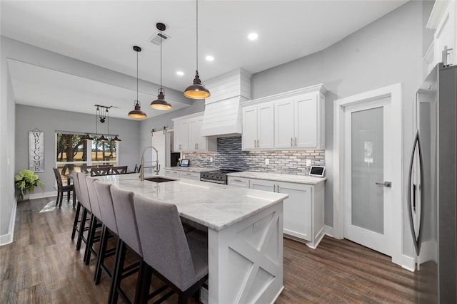 kitchen with appliances with stainless steel finishes, an island with sink, sink, white cabinets, and hanging light fixtures