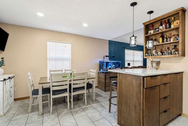 kitchen with hanging light fixtures, light tile patterned flooring, kitchen peninsula, and a kitchen bar