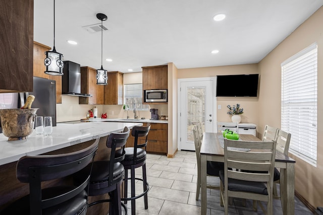 kitchen with hanging light fixtures, appliances with stainless steel finishes, plenty of natural light, and wall chimney exhaust hood