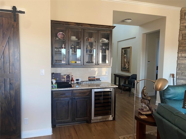 bar with backsplash, wine cooler, dark brown cabinetry, dark hardwood / wood-style flooring, and a barn door