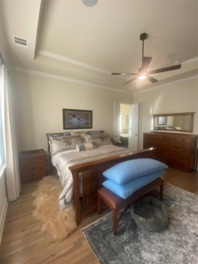 bedroom with hardwood / wood-style flooring, ceiling fan, crown molding, and a raised ceiling