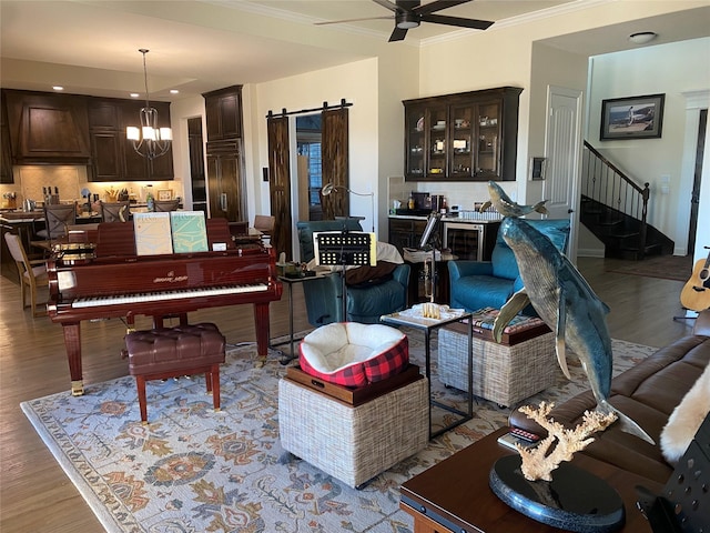 living room featuring crown molding, ceiling fan with notable chandelier, light hardwood / wood-style floors, and a barn door