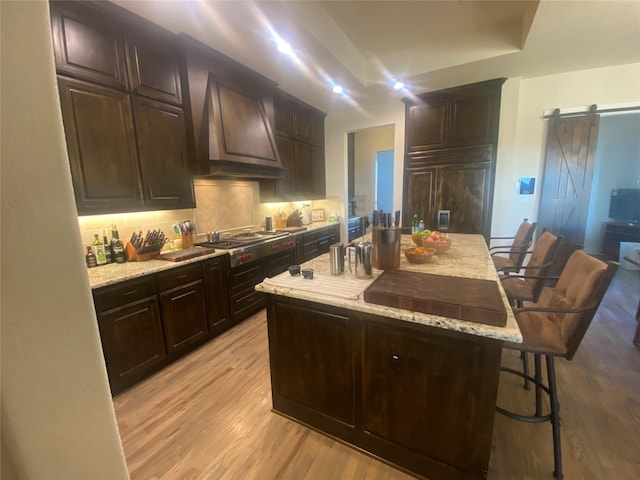 kitchen featuring a kitchen island, a kitchen breakfast bar, stainless steel gas cooktop, a barn door, and custom range hood