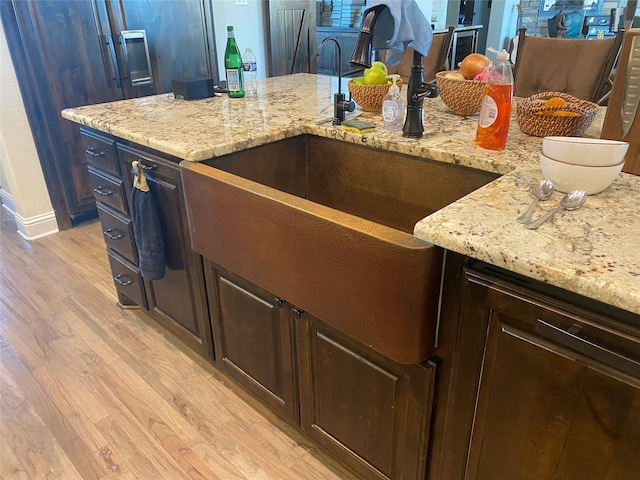 kitchen with dark brown cabinetry, sink, light stone counters, and light wood-type flooring