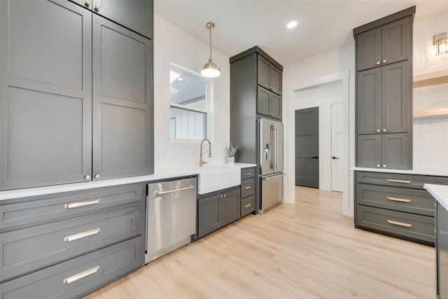 kitchen featuring gray cabinets, appliances with stainless steel finishes, tasteful backsplash, light hardwood / wood-style floors, and decorative light fixtures