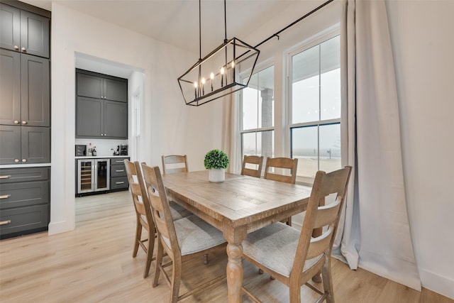 dining area with wine cooler, light hardwood / wood-style flooring, and an inviting chandelier