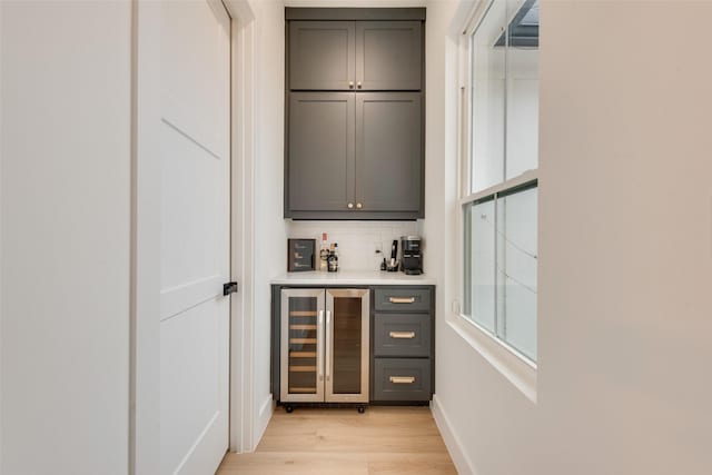 bar featuring wine cooler, light hardwood / wood-style floors, decorative backsplash, and gray cabinetry