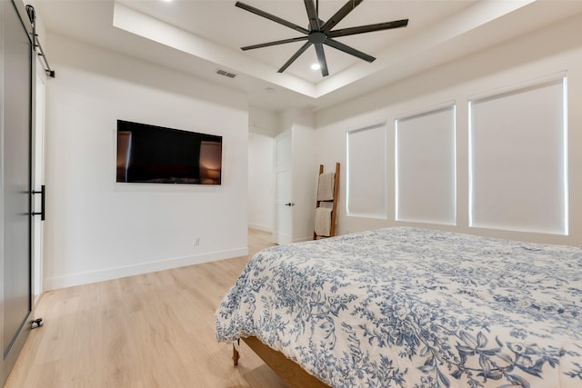 bedroom with hardwood / wood-style flooring, ceiling fan, a tray ceiling, and a barn door