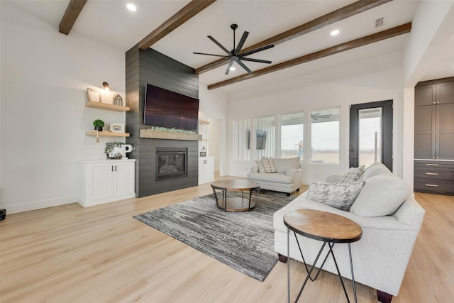 living room featuring beamed ceiling, light hardwood / wood-style flooring, a large fireplace, and ceiling fan