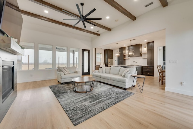 living room with a high ceiling, ceiling fan with notable chandelier, beam ceiling, and light hardwood / wood-style flooring