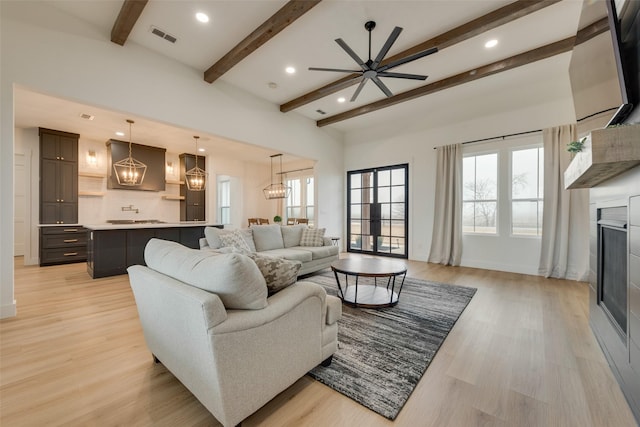 living room with beam ceiling, ceiling fan with notable chandelier, a fireplace, and light hardwood / wood-style floors