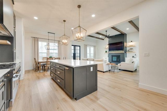 kitchen featuring a kitchen island, stainless steel stove, a fireplace, decorative light fixtures, and light wood-type flooring