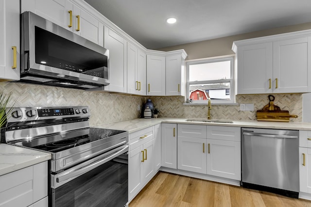 kitchen with sink, white cabinetry, light stone counters, light hardwood / wood-style flooring, and appliances with stainless steel finishes