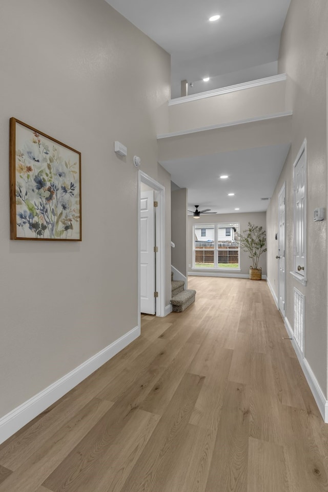 corridor with a towering ceiling and light hardwood / wood-style floors