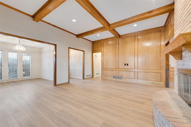 unfurnished living room featuring a notable chandelier, beam ceiling, a brick fireplace, and light hardwood / wood-style flooring