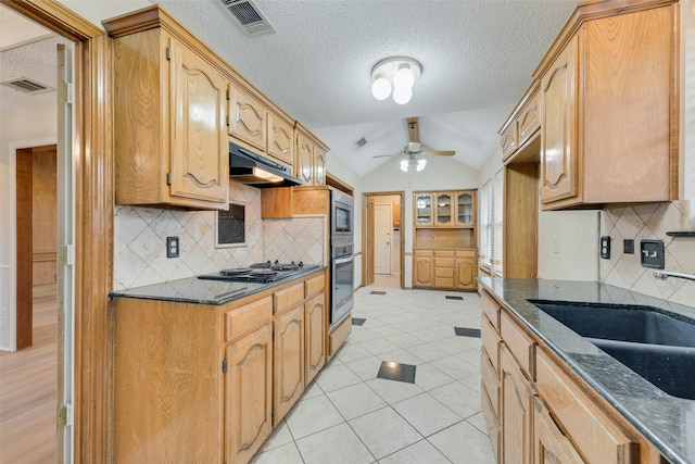 kitchen featuring light tile patterned flooring, sink, vaulted ceiling, ceiling fan, and dark stone counters