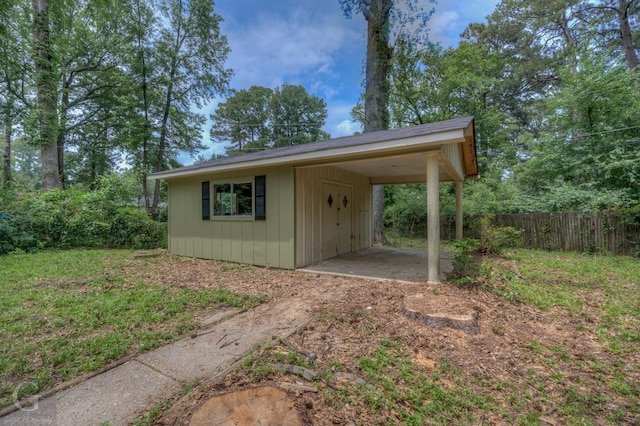 view of outbuilding with driveway, a carport, and fence