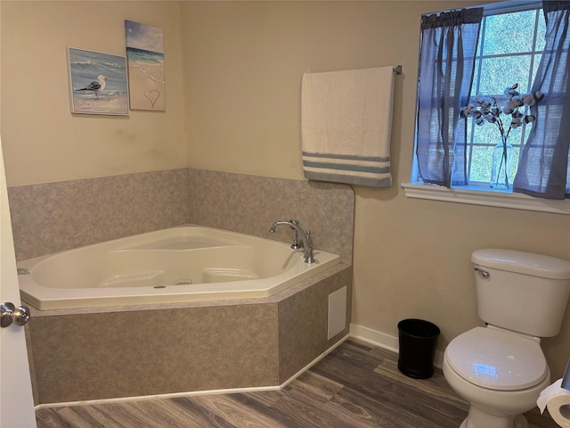 bathroom with tiled tub, plenty of natural light, hardwood / wood-style flooring, and toilet