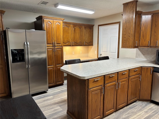 kitchen with stainless steel appliances, kitchen peninsula, a textured ceiling, and light wood-type flooring