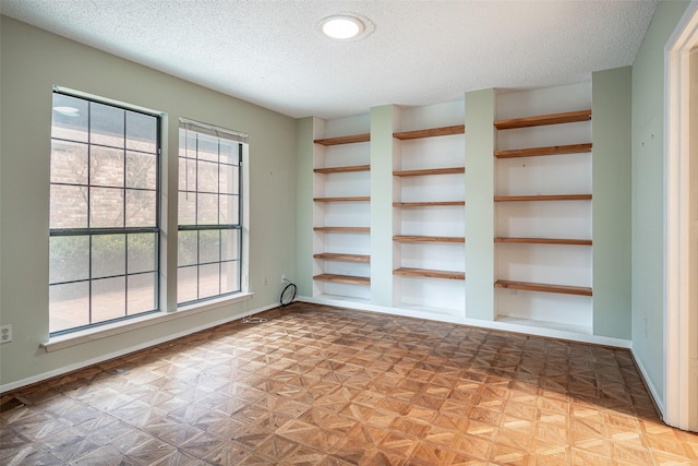 spare room with built in features, a textured ceiling, and light parquet floors