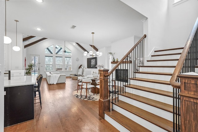 stairs featuring ceiling fan with notable chandelier, hardwood / wood-style floors, and vaulted ceiling with beams