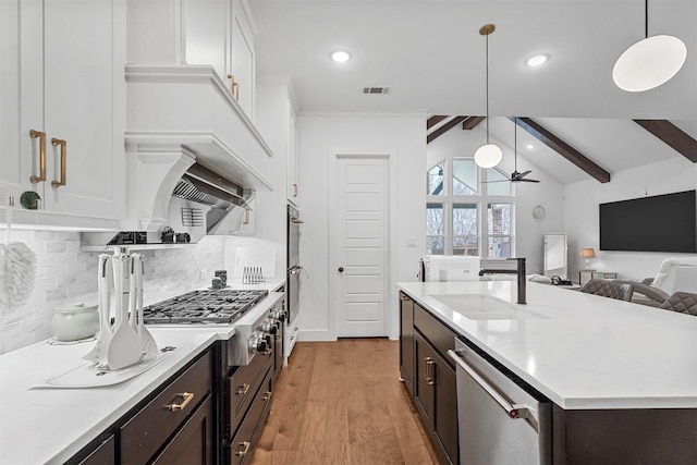 kitchen with hanging light fixtures, stainless steel appliances, sink, and light stone countertops