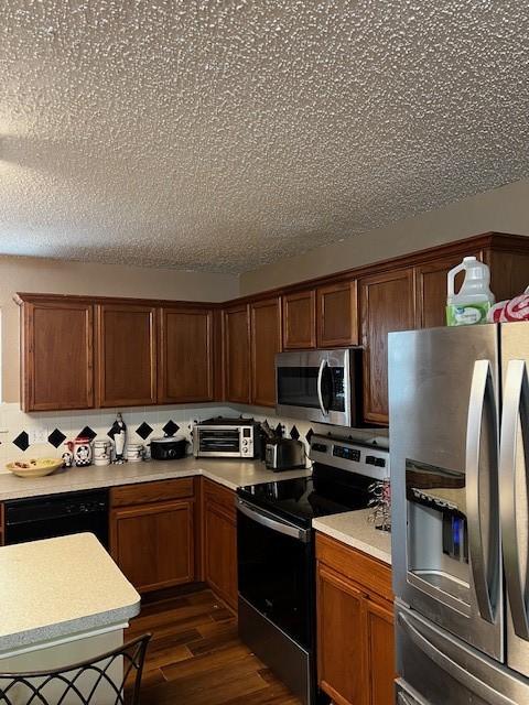 kitchen featuring dark wood-type flooring, decorative backsplash, stainless steel appliances, and a textured ceiling