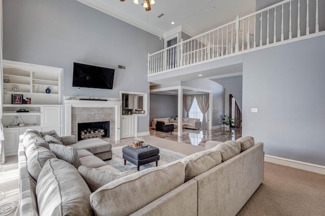 living room featuring a tile fireplace, ceiling fan, a high ceiling, ornamental molding, and light carpet