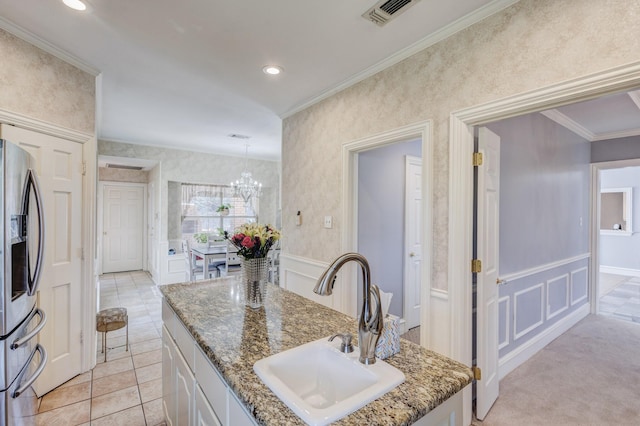 kitchen featuring sink, white cabinetry, stainless steel refrigerator with ice dispenser, ornamental molding, and a center island with sink