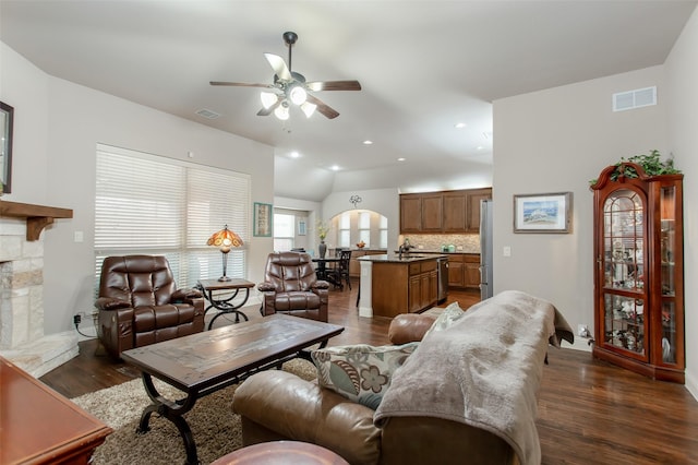 living room with vaulted ceiling, a stone fireplace, dark hardwood / wood-style floors, sink, and ceiling fan