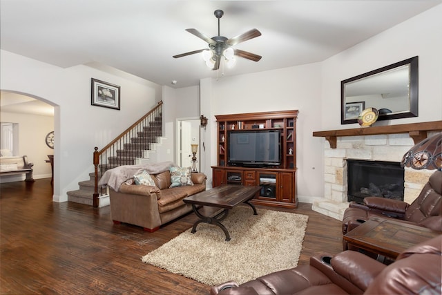 living room with ceiling fan, dark hardwood / wood-style flooring, and a stone fireplace